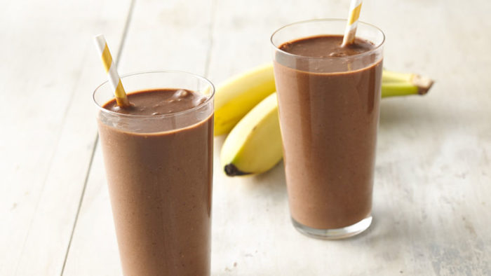 two high-protein chocolate smoothies with a banana in the background